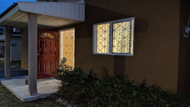 A house with a wooden door, a window with a grid pattern, and a covered porch. - Island Away – 2 Bedroom Nestled in Angel Estate, Near Kingston & Ocho Rios (Angels Estate)