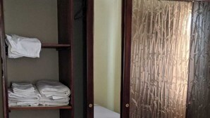 A bedroom with a bed, a wardrobe with folded towels, and a door with a bamboo pattern. - Island Away – 2 Bedroom Nestled in Angel Estate, Near Kingston & Ocho Rios (Angels Estate)
