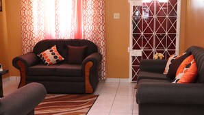 A living room with two sofas, a patterned curtain, and a tiled floor. - Island Away – 2 Bedroom Nestled in Angel Estate, Near Kingston & Ocho Rios (Angels Estate)