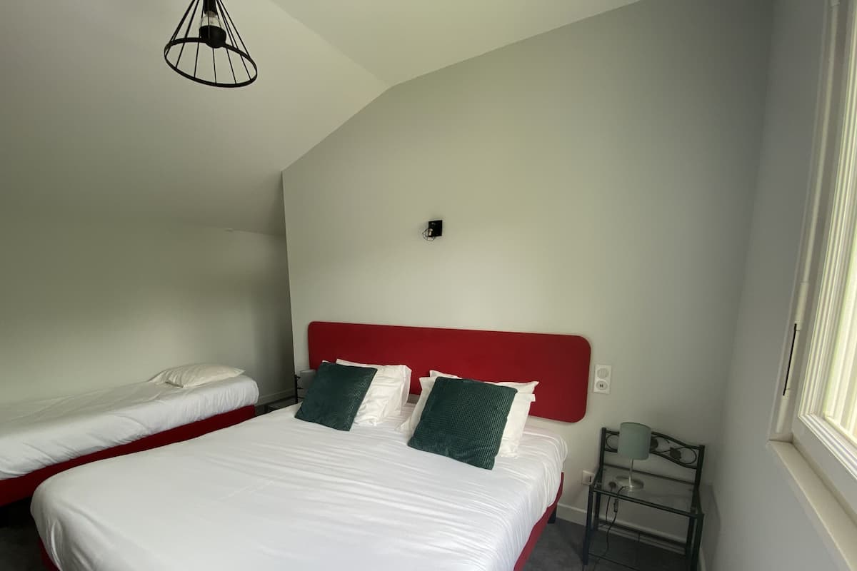 A bedroom with a large bed, a smaller bed, a red headboard, a bedside table, and a hanging light fixture.