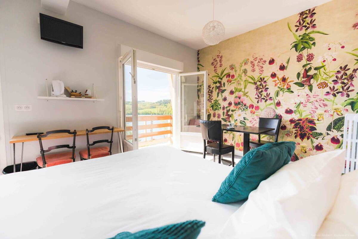 A bedroom with a large bed, a desk with chairs, a television, and a mural of flowers.