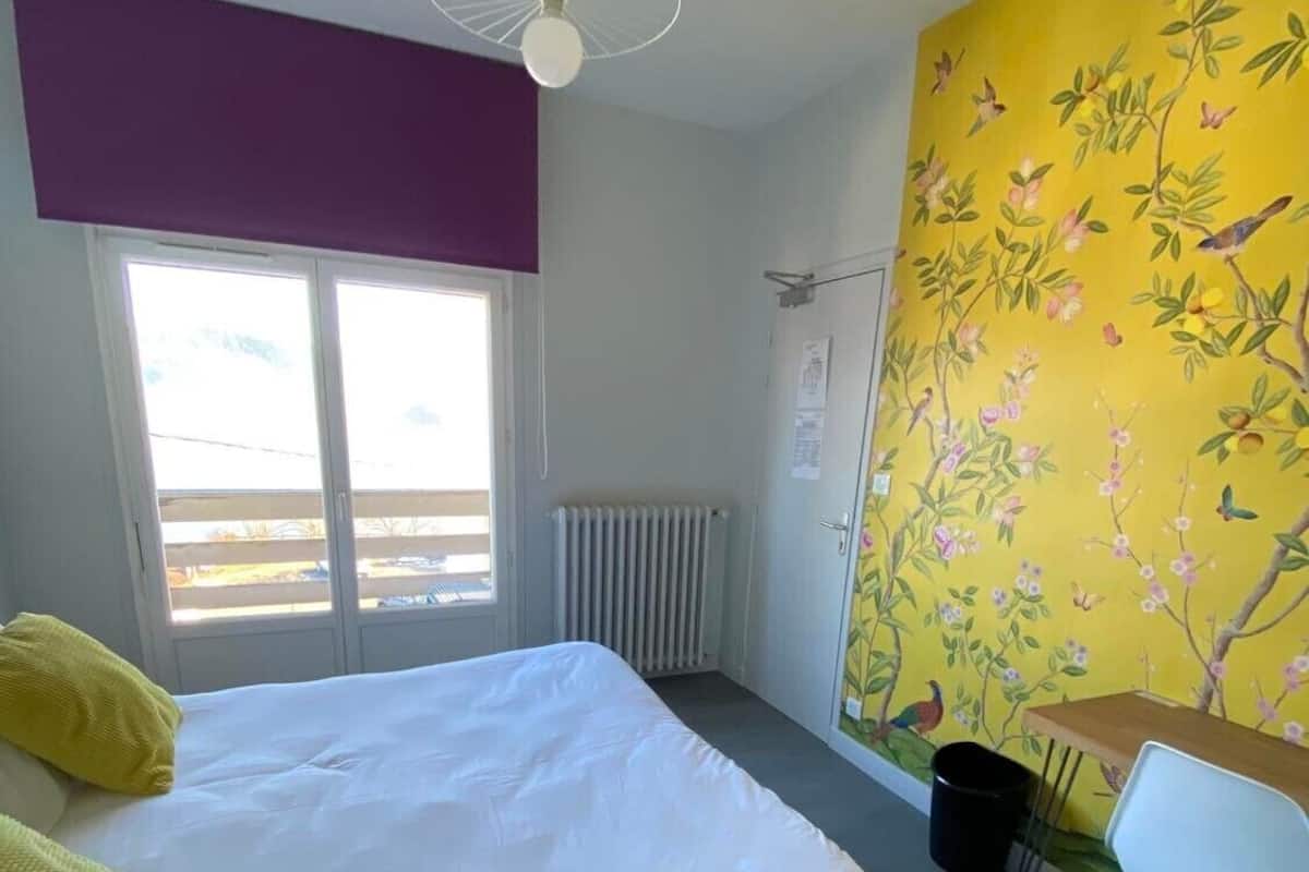 A bedroom with a bed, a window, a radiator, a desk, and a chair.