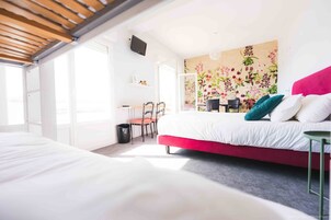 Un dormitorio moderno con una cama grande, un escritorio y una silla. Hay una ventana que proporciona luz natural y una pared con un mural floral.