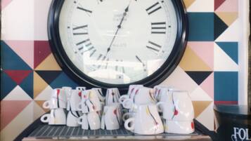 Een wandklok met Romeinse cijfers en een koffieapparaat met diverse knoppen eronder.
