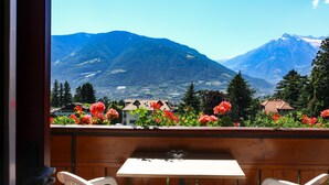 Un balcon avec une table et des chaises, donnant sur un paysage montagneux parsemé de fleurs rouges et surplombant un village.