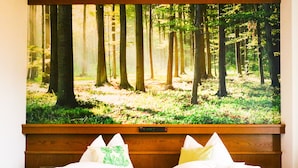 Une chambre à coucher avec un grand tableau sur le thème de la forêt au mur, une tête de lit en bois et un lit avec du linge de lit blanc et des coussins décoratifs.