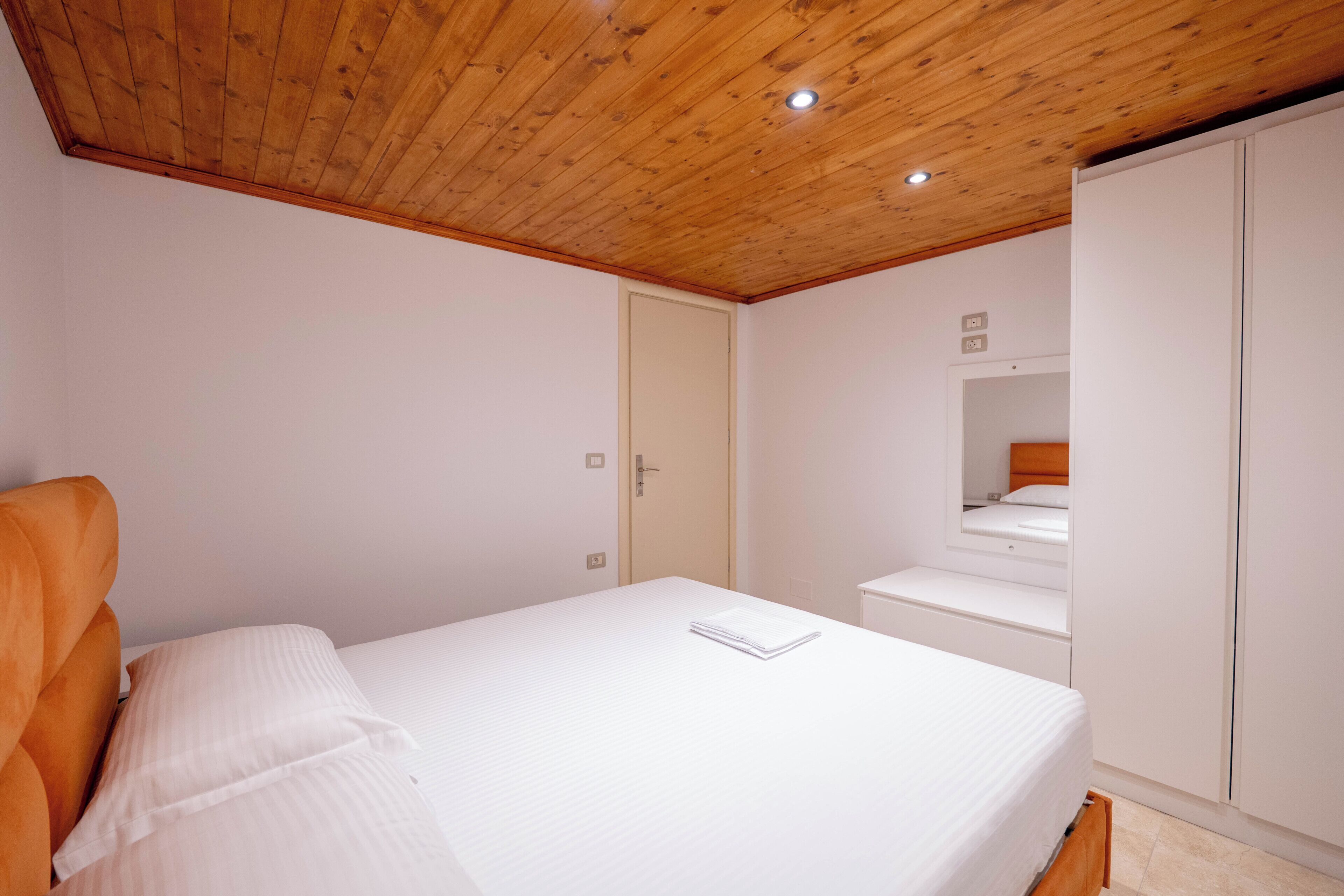 Um quarto com teto de madeira, uma cama, um guarda-roupa e uma porta.