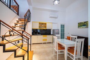 A modern kitchen with a dining area, wooden staircase, and a view of the outdoors.
