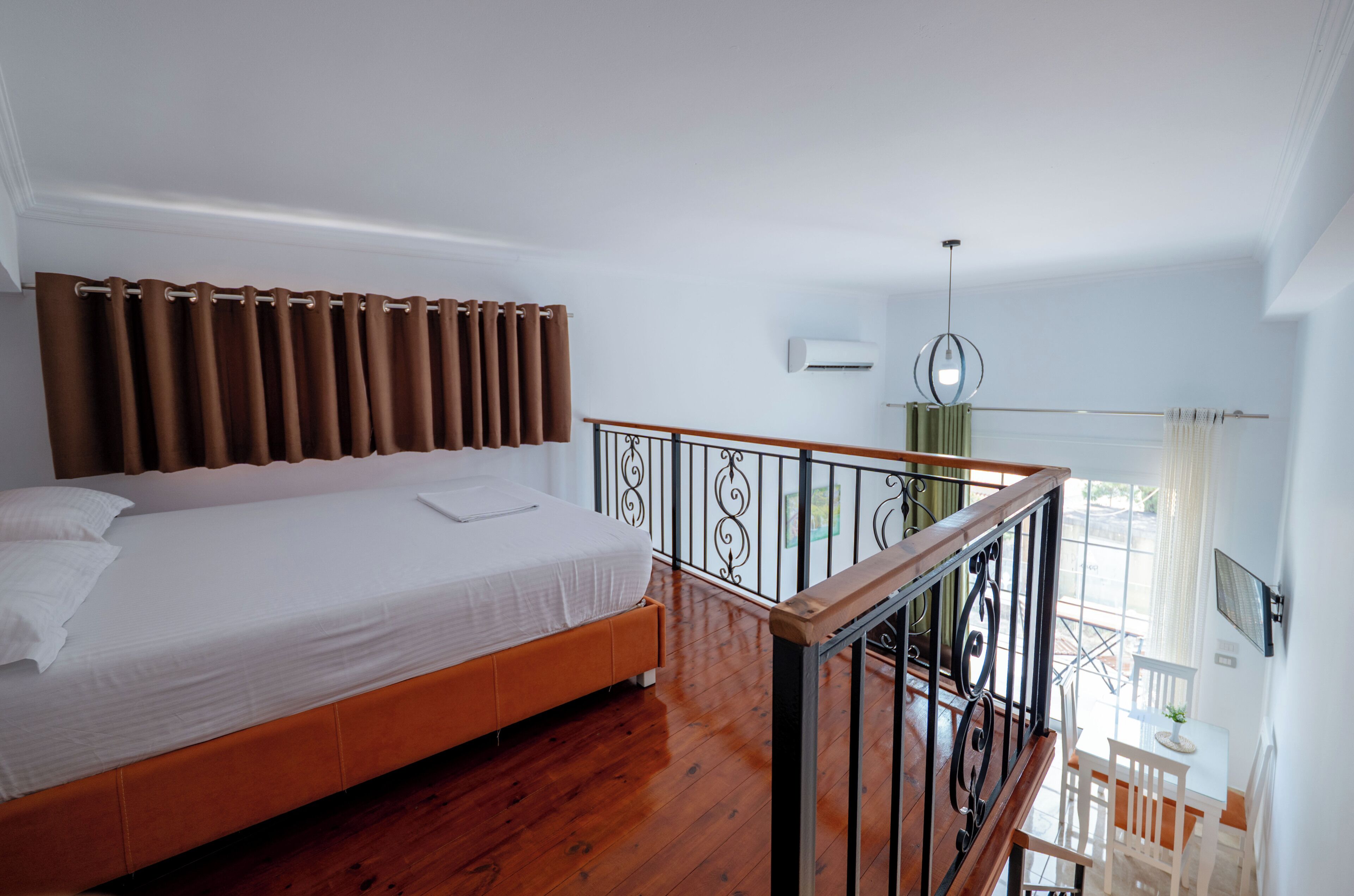 A bedroom with a wooden bed, a balcony with a railing, and a view of the outdoors.