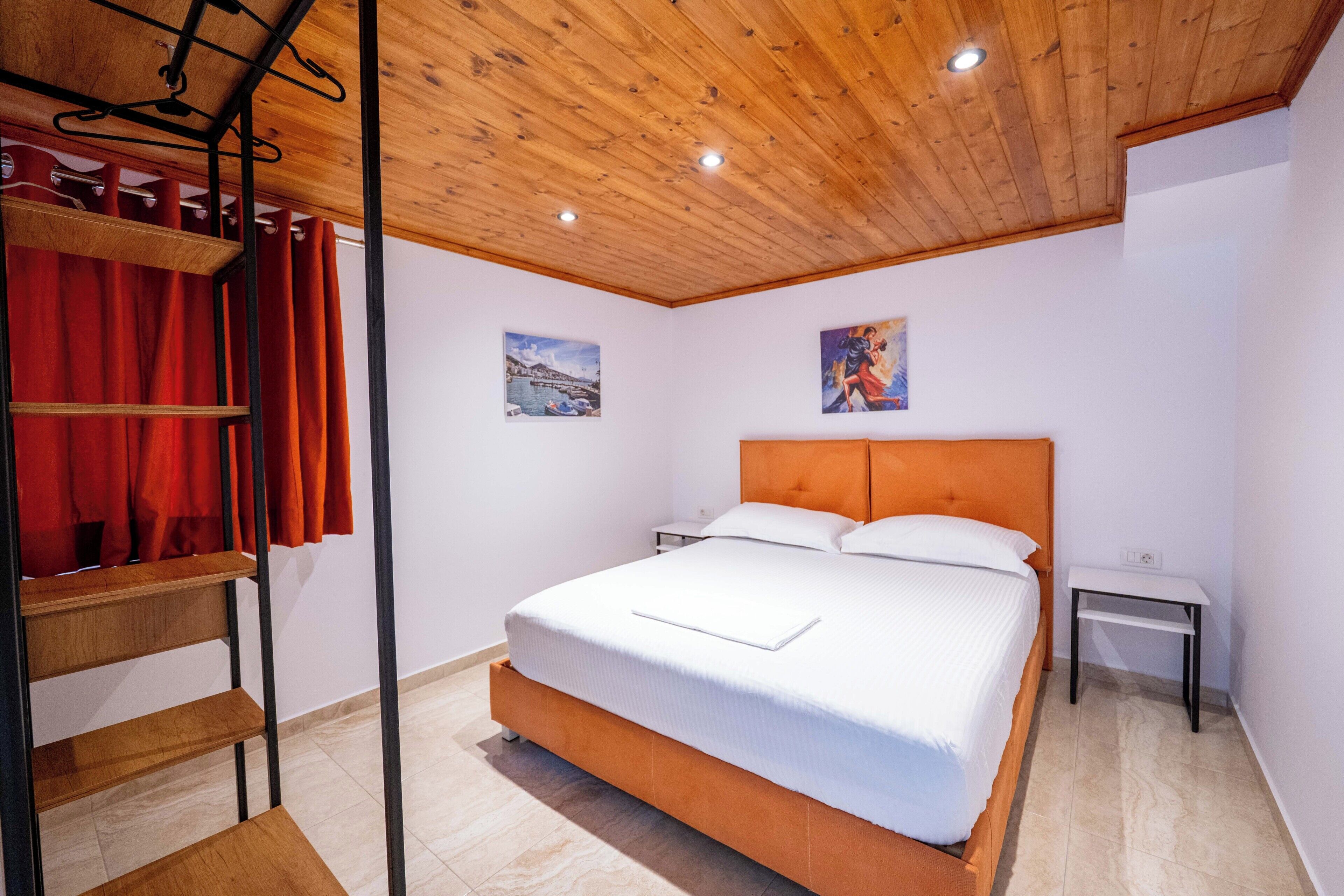 Une chambre avec un plafond en bois, un lit avec une literie blanche, une tête de lit en bois, une table de chevet et un rideau rouge.