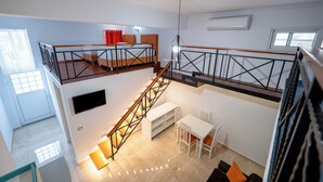 A multi-level room with a staircase, a bed, a dining area, and a TV mounted on the wall.
