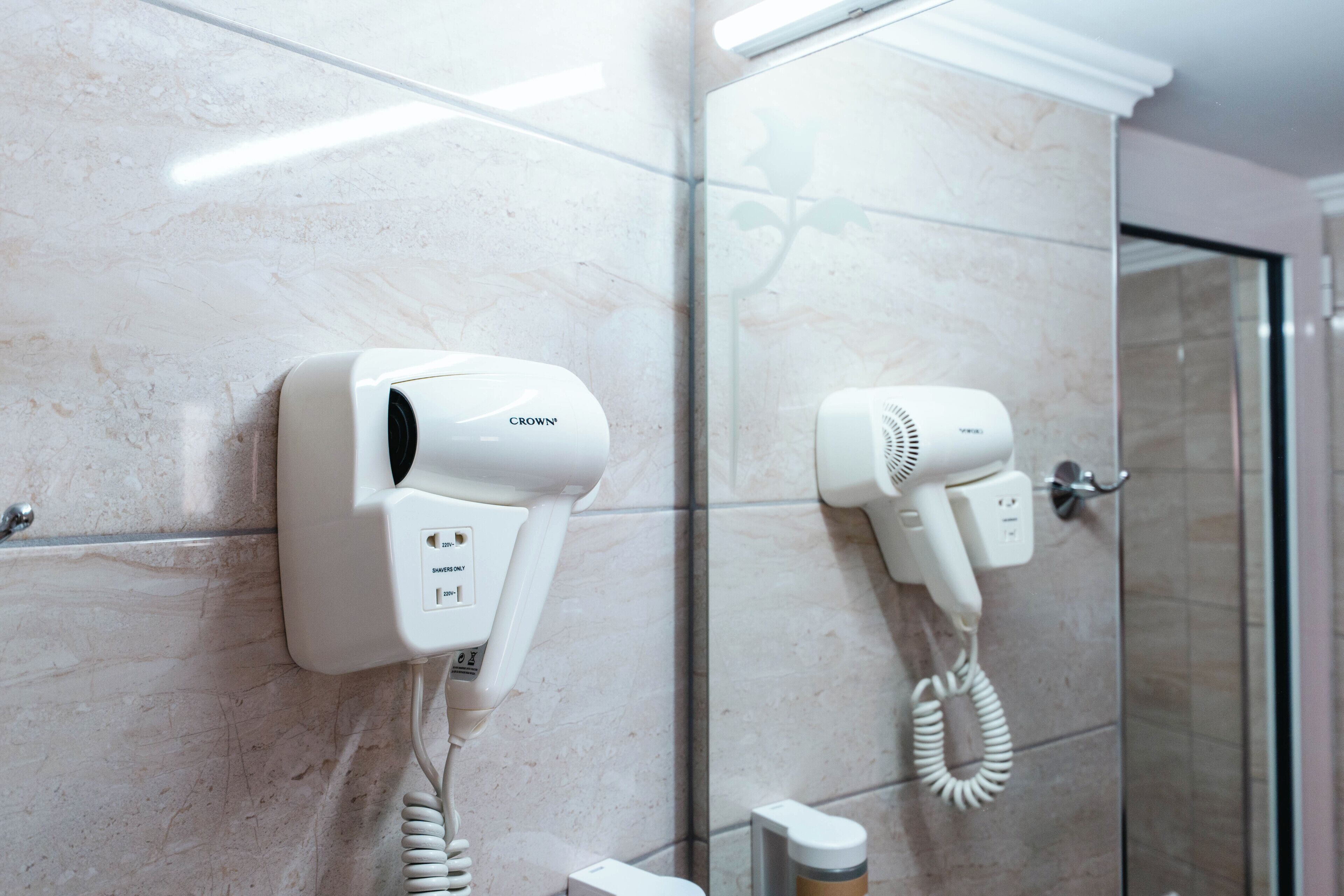 A bathroom with two hair dryers mounted on the wall, a glass shower door, and a marble floor.