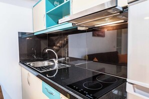 A modern kitchen with a black countertop, stainless steel sink, and a built-in stove. - Crown Deluxe Apartments (Sarande)