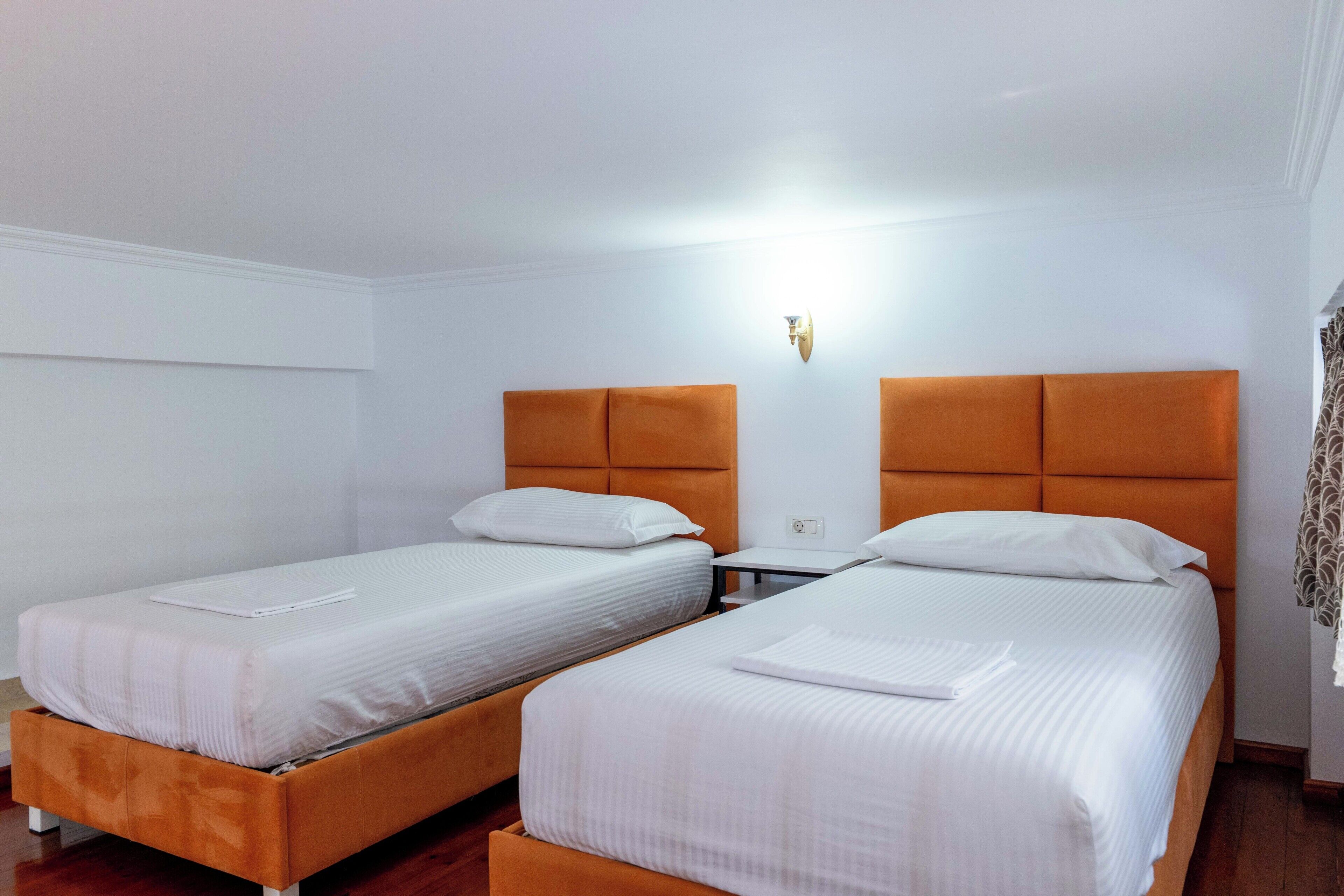 A hotel room with two beds, white bedding, and an orange headboard.