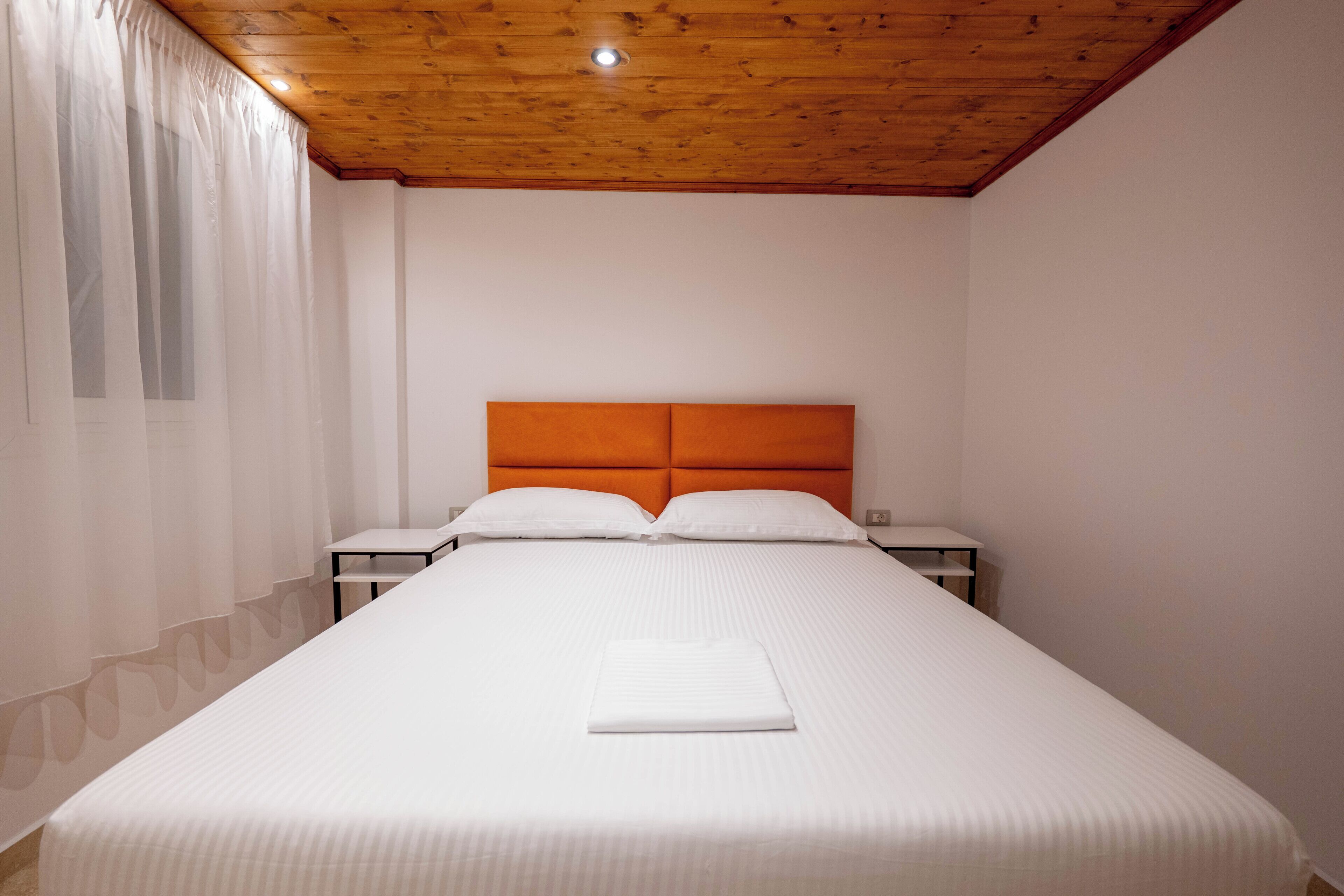 A hotel room with a wooden ceiling, a large bed with white bedding, two bedside tables, and a nightstand.