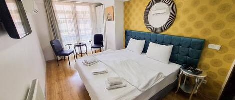 A hotel room with a large bed, a blue headboard, a round mirror, and a small table with a chair.