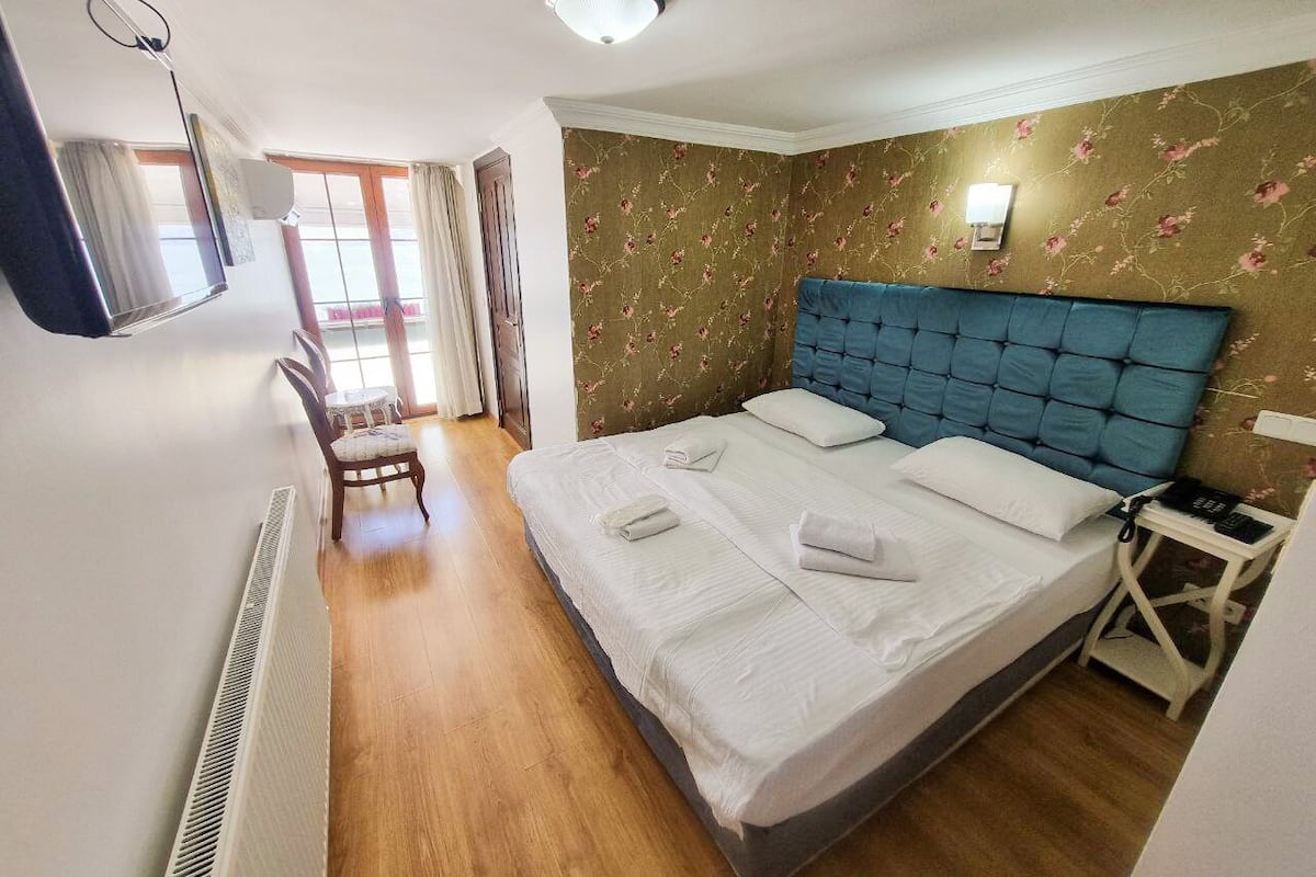 A hotel room with a large bed, a bedside table, a chair, a TV, and a window with curtains.