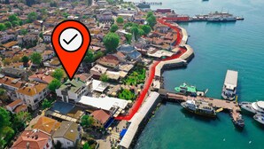 An aerial view of a coastal town with a prominent red pathway along the waterfront, a mosque with a dome, and various buildings and boats. - My Way Teras Butik Otel (Adalar)