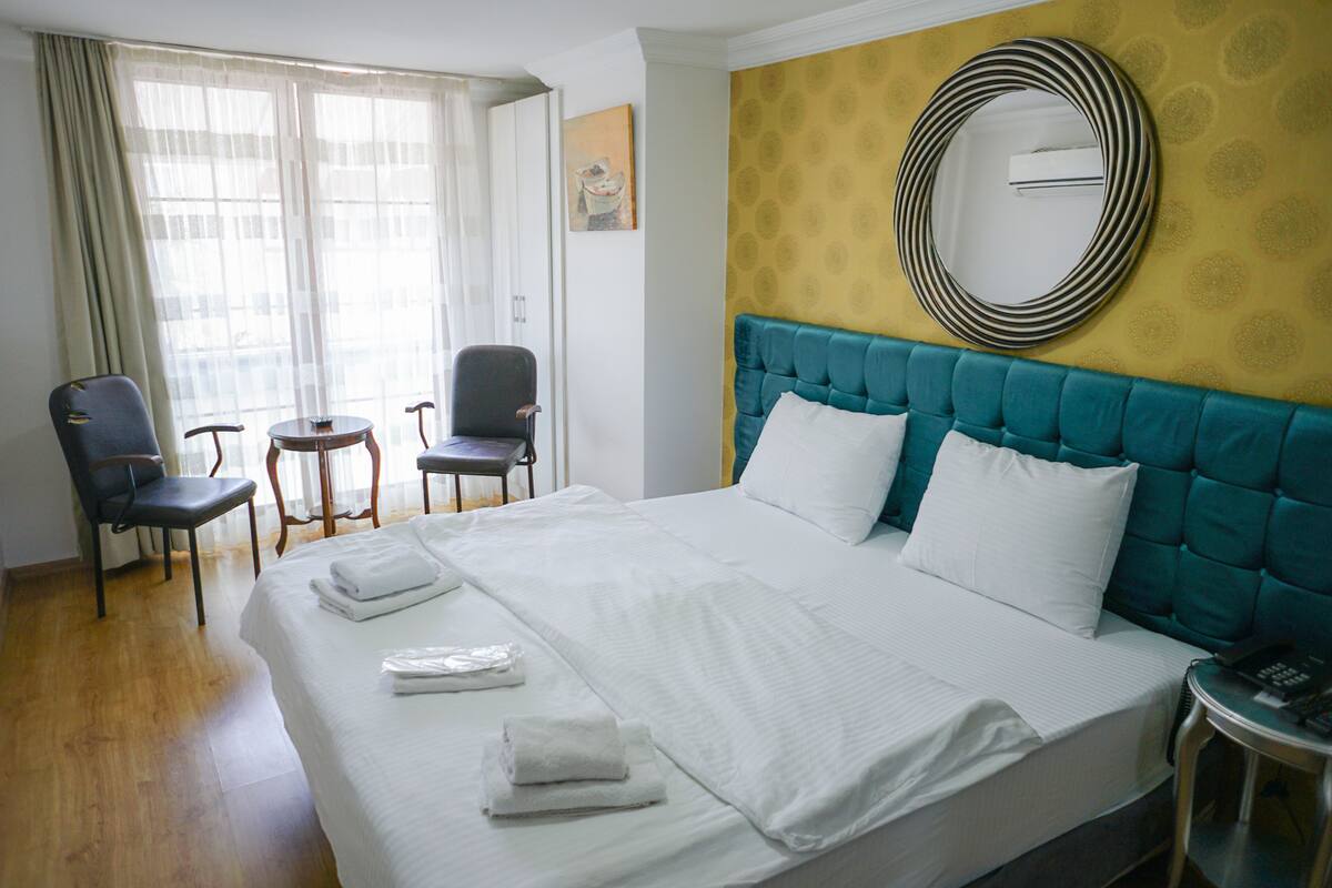 A hotel room with a large bed, two chairs, a small table, and a round mirror on the wall.