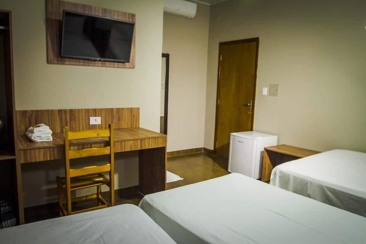 A hotel room with two beds, a desk with a chair, a television mounted on the wall, and a door.