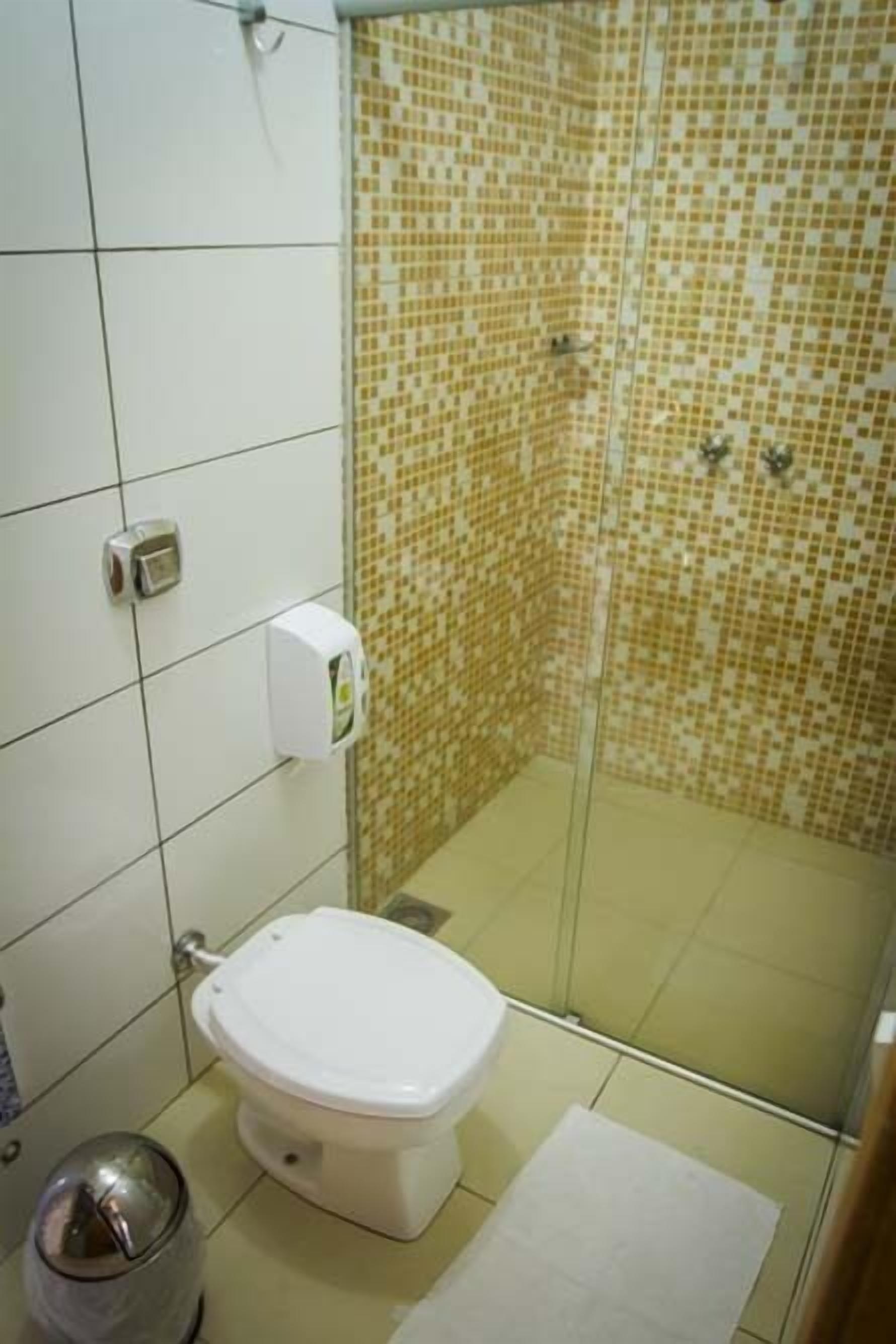 A bathroom with a toilet, a trash bin, a hand dryer, and a shower with mosaic tiles.