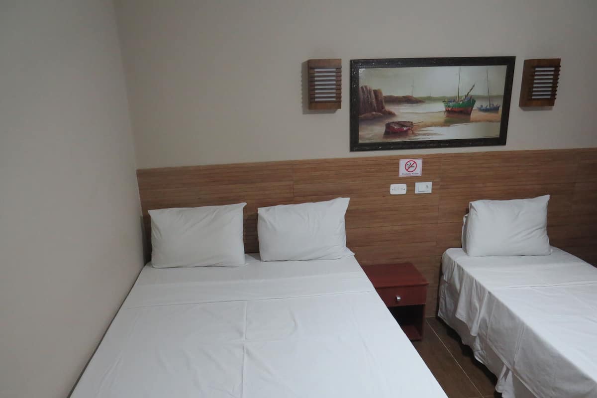 A hotel room with two single beds, a wooden headboard, a painting of boats on the wall, and a no-smoking sign.