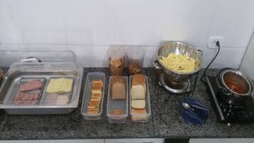 A kitchen counter with various food items and containers, including trays of meats, bread, and a bowl of potatoes.
