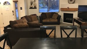 A living room with a sectional sofa, a fireplace, a television, and a dining table.