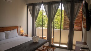 Habitación de hotel con cama, un banco de madera, una mesa con lámpara y vista a zonas verdes por la ventana.