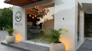 Un edificio moderno con entrada de vidrio, plantas en macetas y un logotipo en la pared.
