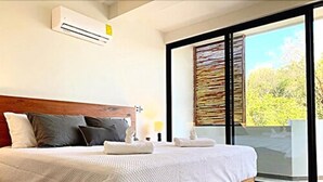 Un dormitorio con cama de madera, ropa de cama blanca, un ventanal grande y un equipo de aire acondicionado.