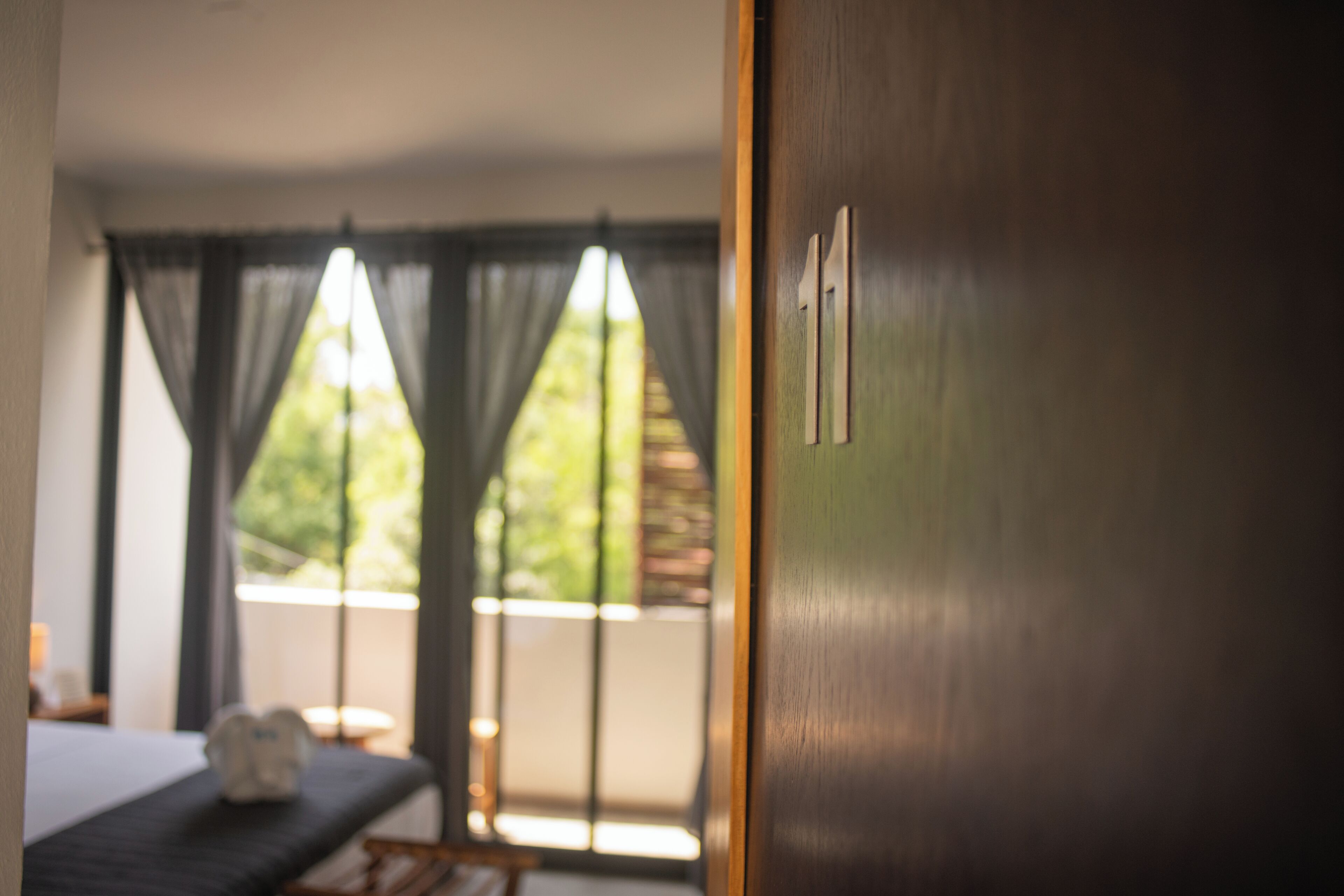 A room with a bed, a nightstand, and a view through a window with curtains.