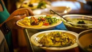 Eine Person hält einen Teller mit verschiedenen Speisen, darunter ein Salat und Suppe, an einem Buffet.