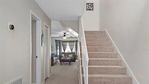 Un escalier menant à un salon équipé d’un ventilateur de plafond, d’un canapé et d’une table basse.