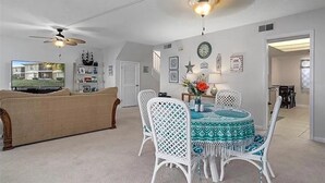Un coin repas avec une table ronde, des chaises blanches et un ventilateur de plafond.
