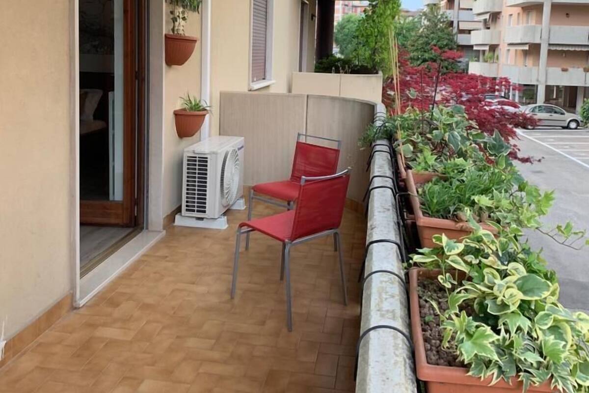 A balcony with a red chair, a potted plant, and an air conditioning unit.