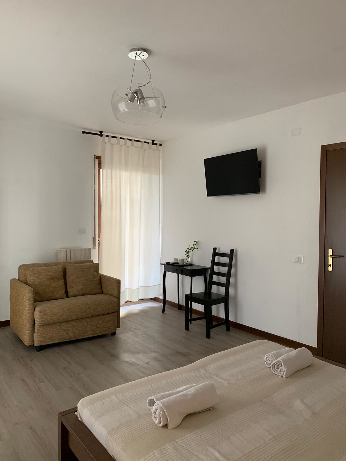 A hotel room with a sofa, a desk with a chair, a TV mounted on the wall, and a bed with towels.