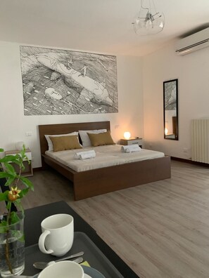 A modern bedroom with a large bed, a bedside table, a nightstand, a wall-mounted mirror, and a large abstract artwork. - Nottetempo Verona (Verona)