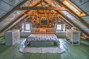 Une chambre mansardée avec un plafond en pente, un lit recouvert d’un tapis blanc et moelleux, deux tables de chevet et un miroir au-dessus du lit.