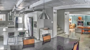 Une cuisine moderne dotée d’un îlot central, d’appareils électroménagers en acier inoxydable et de luminaires suspendus.