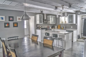 Une cuisine moderne avec des meubles blancs, un îlot central et un coin repas comprenant une grande table et des chaises.