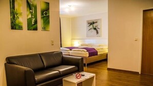 Uma sala de estar moderna com um sofá de couro preto, uma mesinha lateral branca e uma cama com cabeceira branca.
