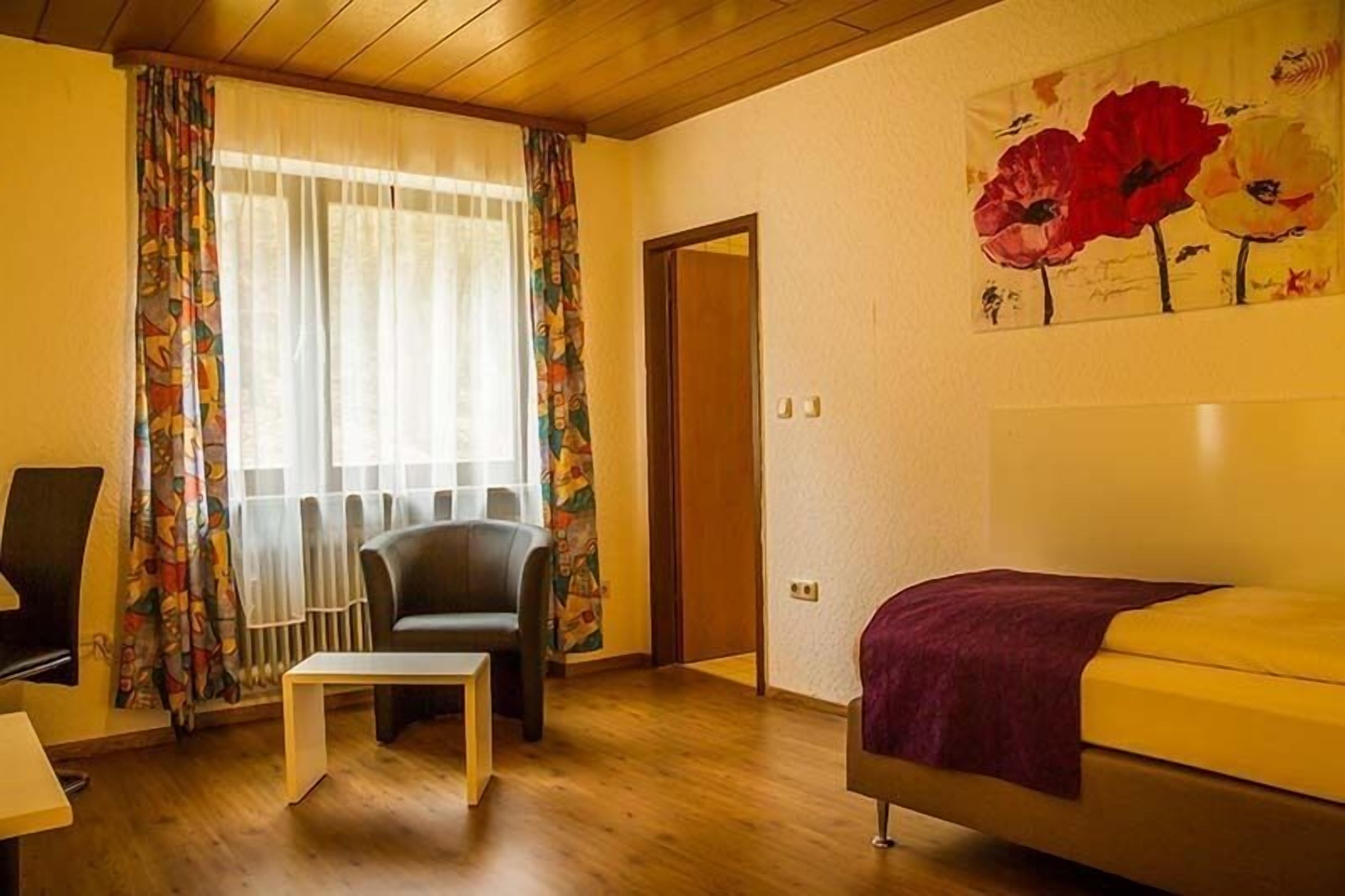 Una habitación con cama, una silla, una mesita y una ventana con cortinas.