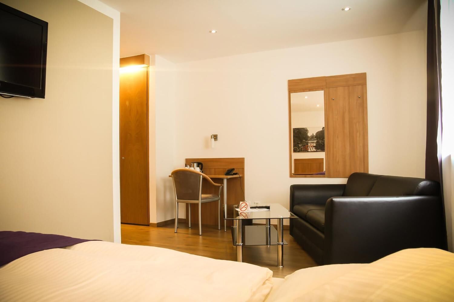 Een hotelkamer met een bed, een slaapbank, een bureau met stoel, een aan de muur bevestigde televisie en een raam met uitzicht.