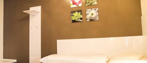Quarto com cama branca, mesa de cabeceira branca, parede marrom e quatro quadros emoldurados.
