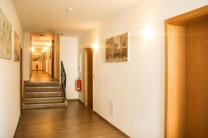 Um corredor com piso de madeira, escada e um extintor fixado na parede.