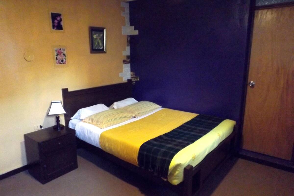 A bedroom with a bed, a nightstand, a lamp, and a door.