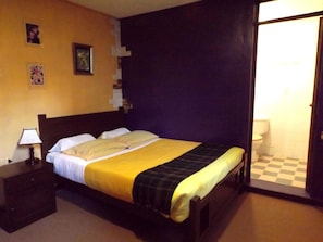 A hotel room with a bed, a nightstand, a lamp, and a checkered floor. - El Manzano Hostel (Puno)