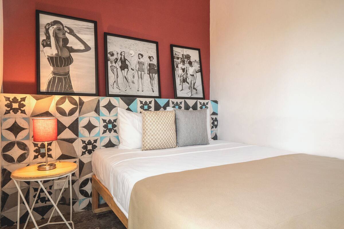 Een hotelkamer met een bed, een nachtkastje met een lamp, en drie ingelijste foto's aan de muur.