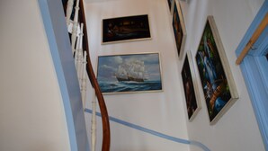 Een trap met een leuning, een schilderij van een zeilschip, en een lijst met een foto aan de muur.